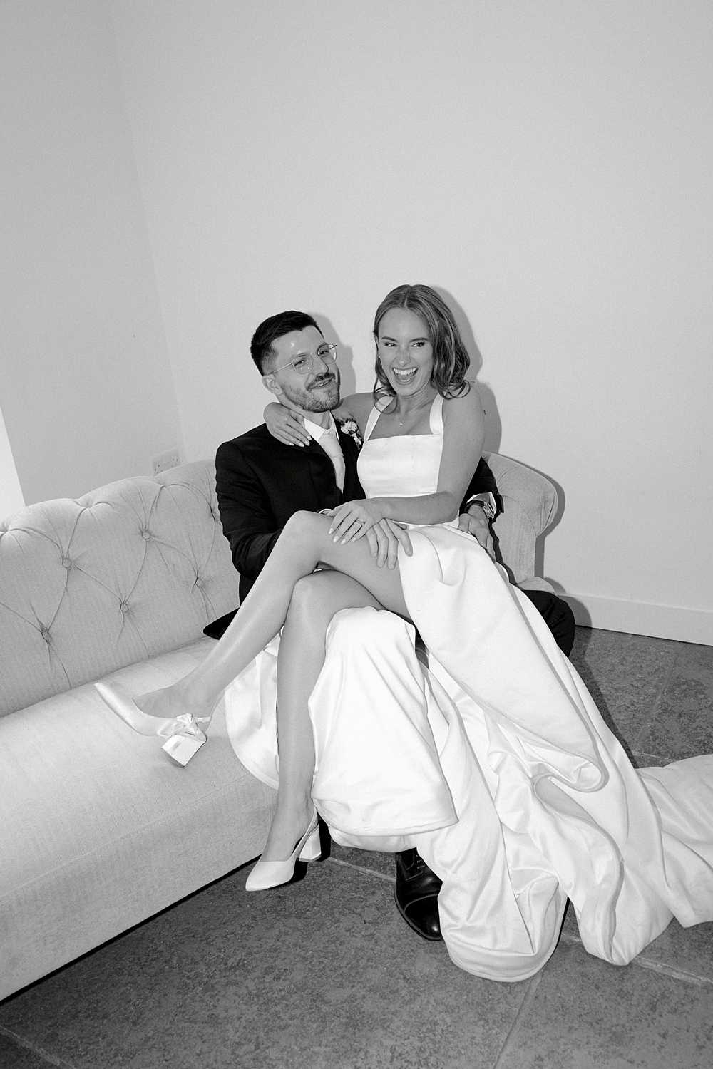 Black and white editorial portrait of a bride and groom relaxing on a sofa at their luxury wedding at Aswarby Rectory in the UK