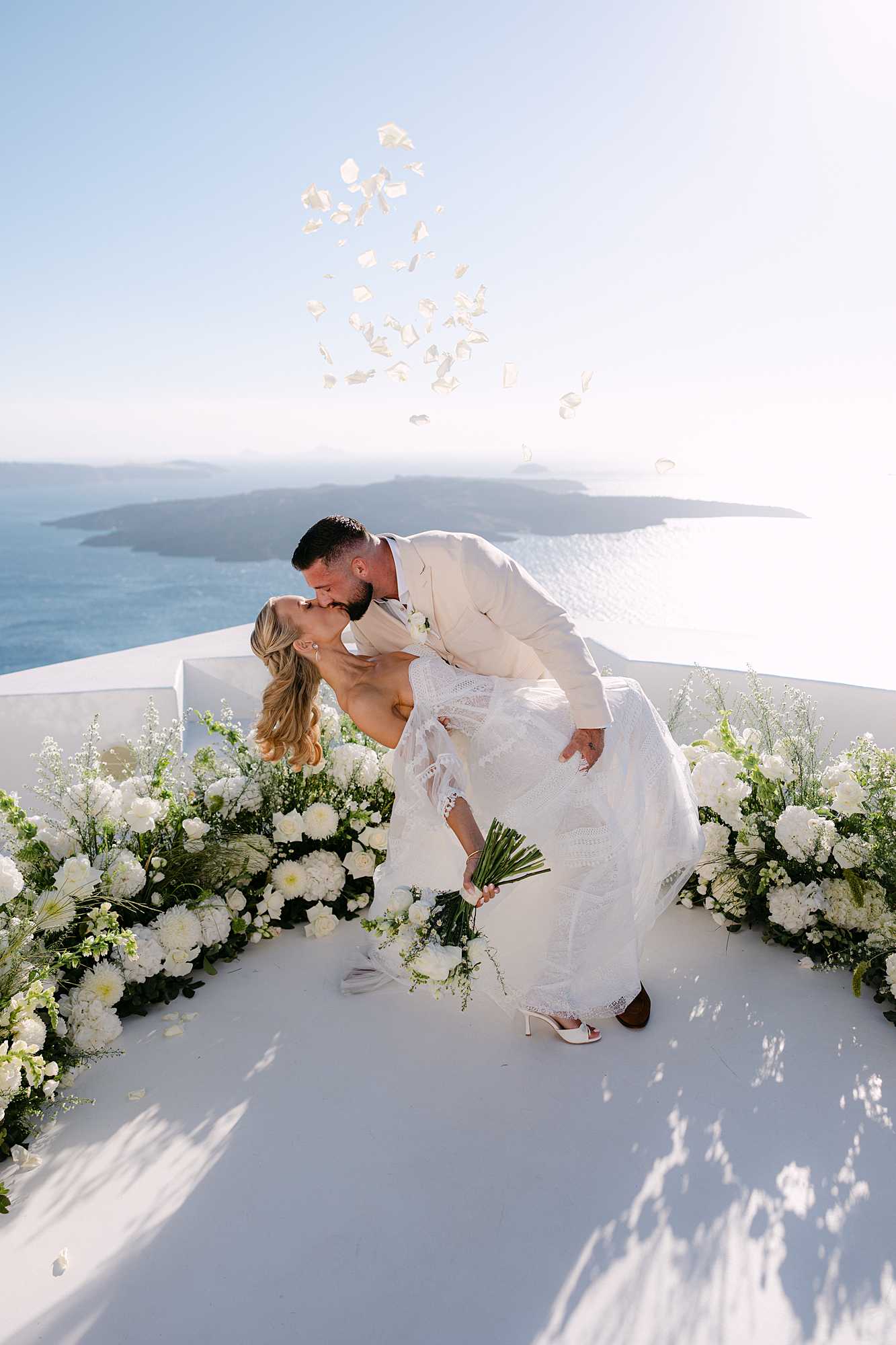 Bride and groom kissing on a whitewashed terrace at Dana Villas, Santorini, overlooking the caldera.