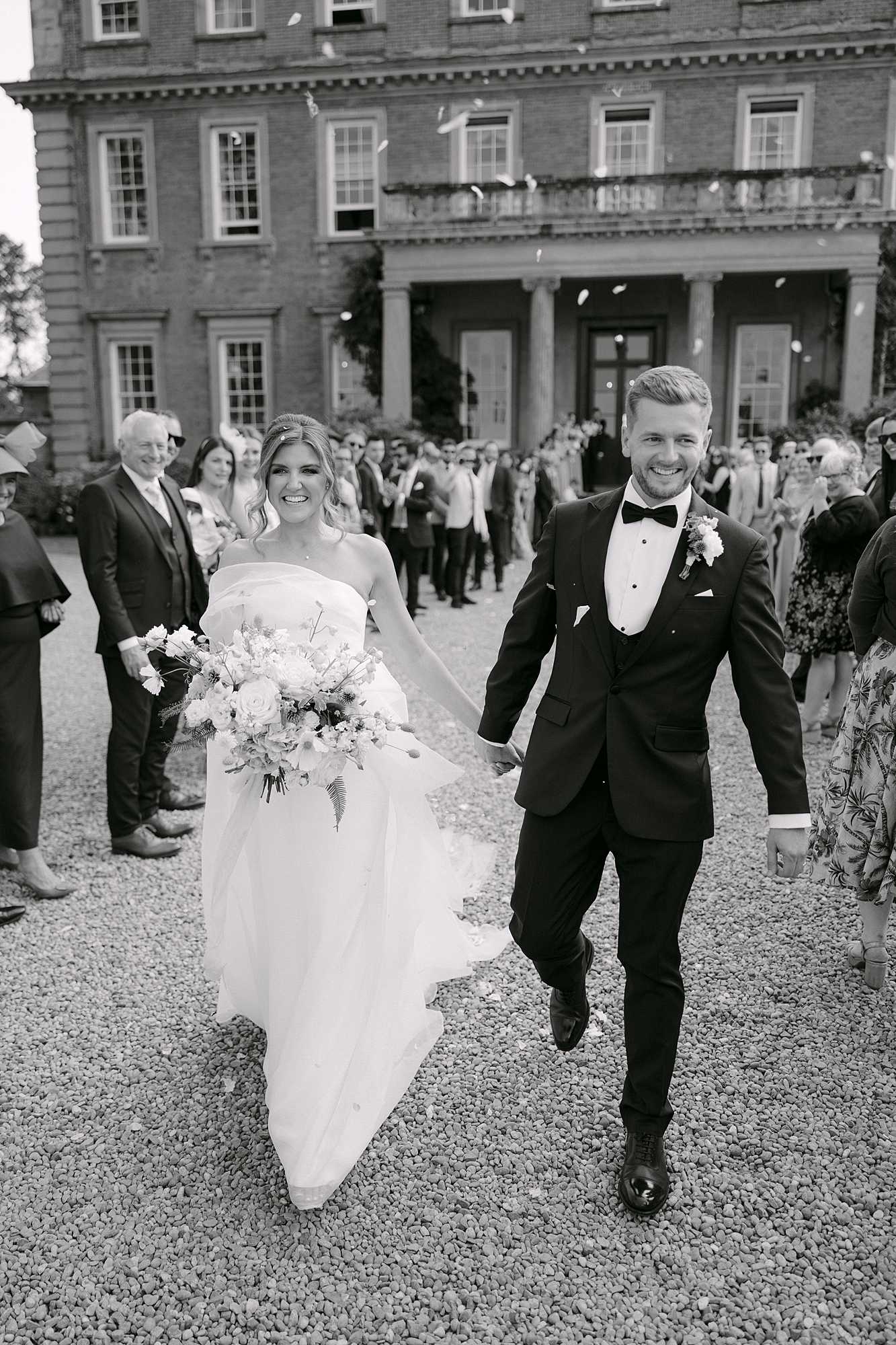 Bride and groom walking hand in hand through confetti outside Davenport House after their wedding ceremony.