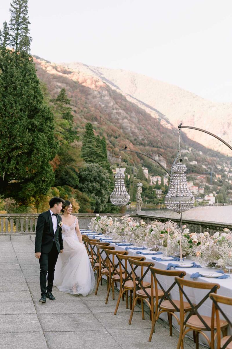 Editorial Lake Como wedding at Villa Pizzo with a couple walking beside a luxury floral tablescape overlooking the mountains.