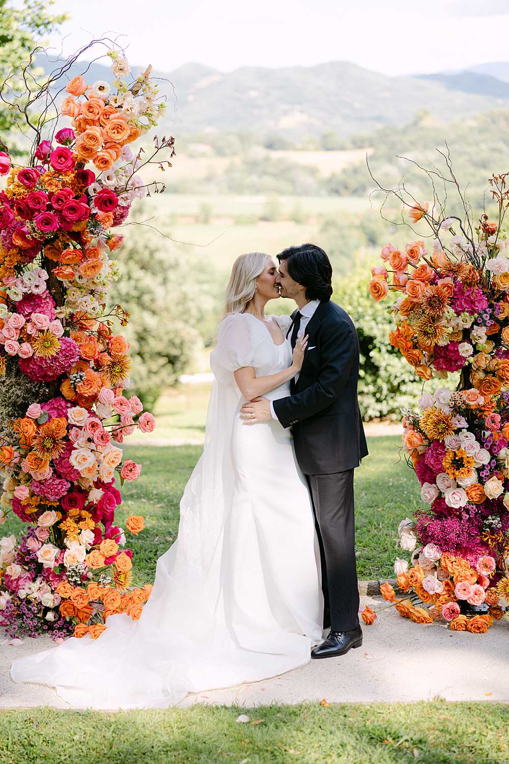 Bride and groom sharing a kiss beneath a floral arch at an intimate Villa Atena wedding in the Tuscan countryside.